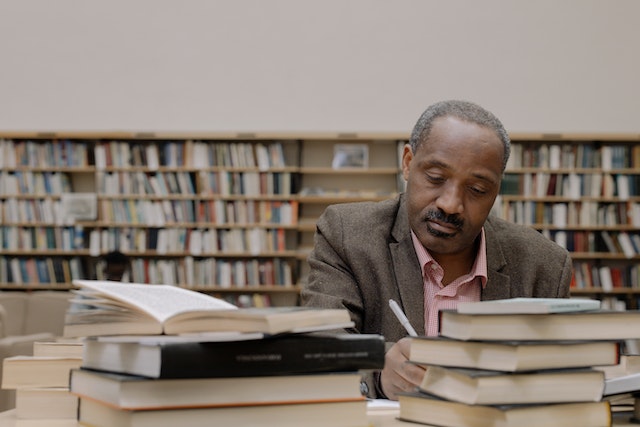 https://www.pexels.com/photo/man-in-gray-suit-jacket-sitting-beside-books-6334771/