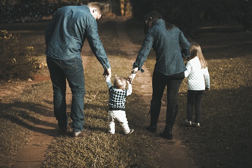 Familia con dos críos. Los padres están ayudando a andar al bebé