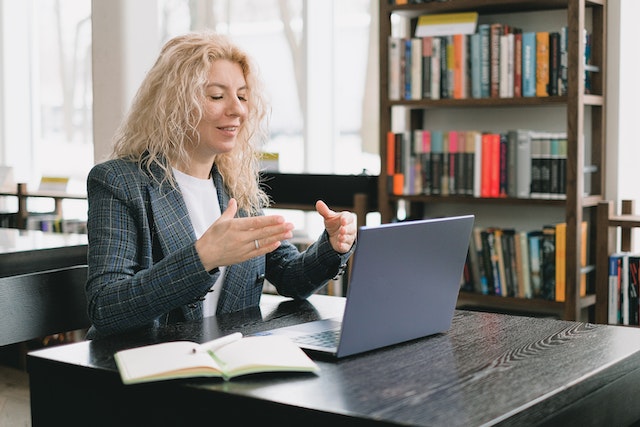 https://www.pexels.com/photo/smiling-woman-having-video-chat-via-laptop-in-library-7516347/